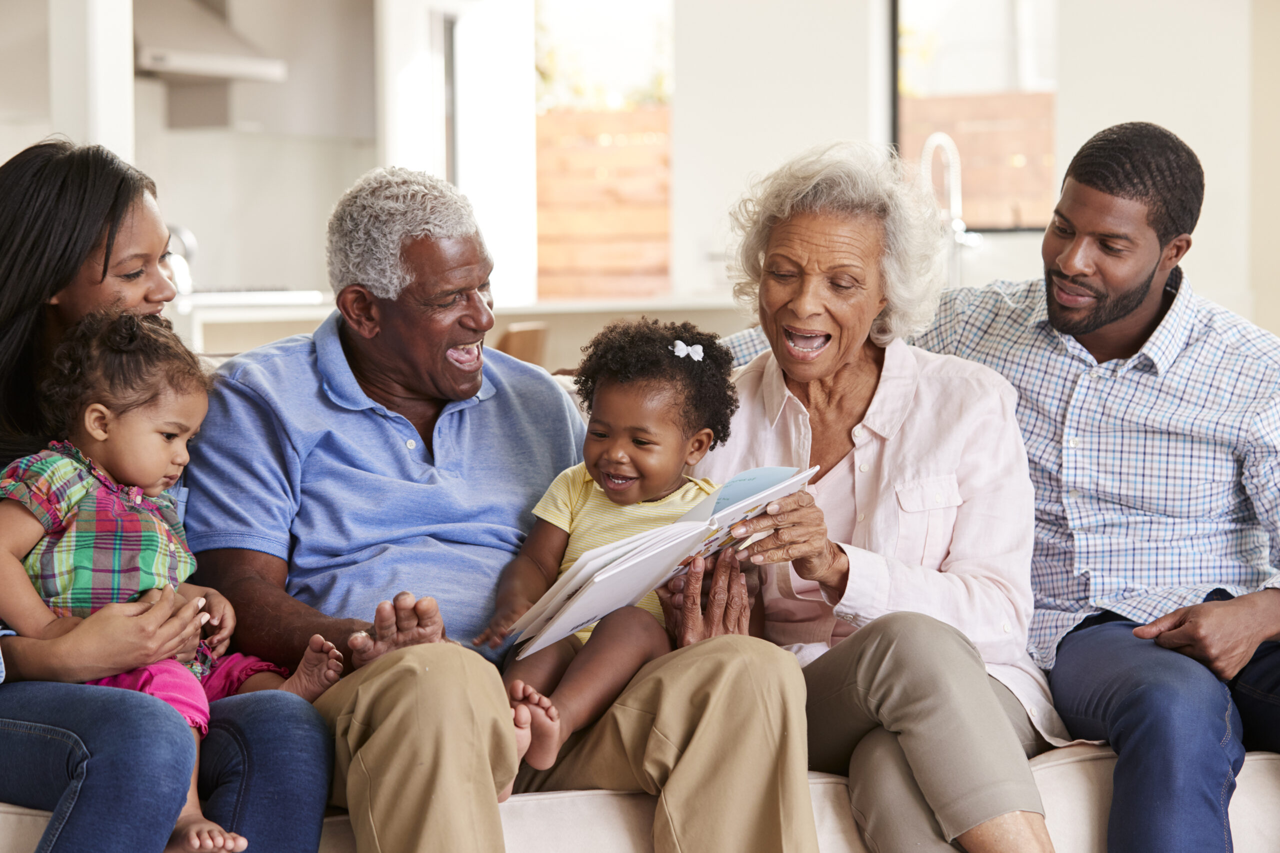Multi-generational family reading together on a couch, grandparents and parents sharing a story with children at home