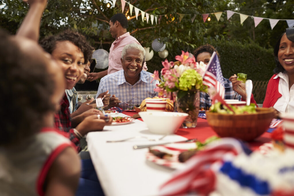 Multi-generational Black family gathered around an outdoor table during a Memorial Day celebration with patriotic decorations and shared meal