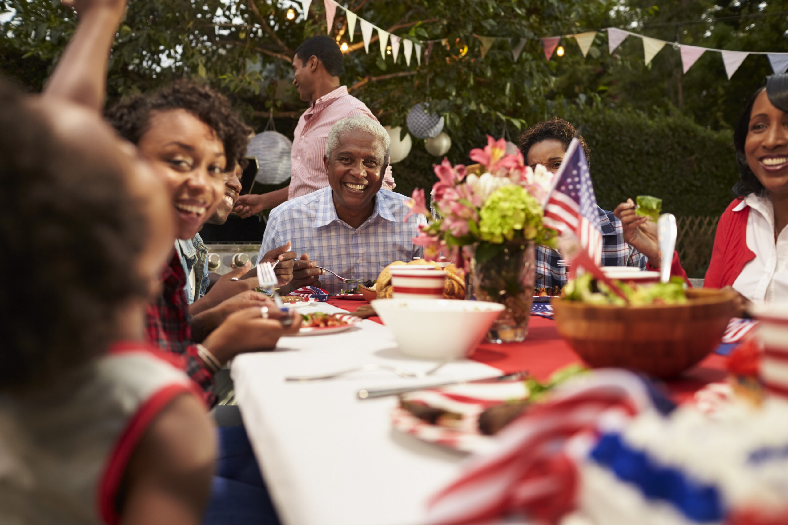 Multi-generational Black family gathered around an outdoor table during a Memorial Day celebration with patriotic decorations and shared meal