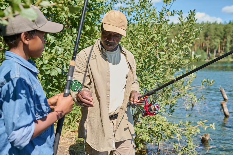Adult teaching a child how to fish by a lake, celebrating Black fishing heritage, family traditions, and outdoor recreation.