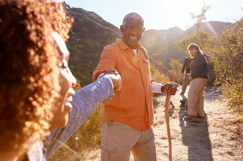 Black hikers helping each other on a nature trail during a group outdoor adventure.